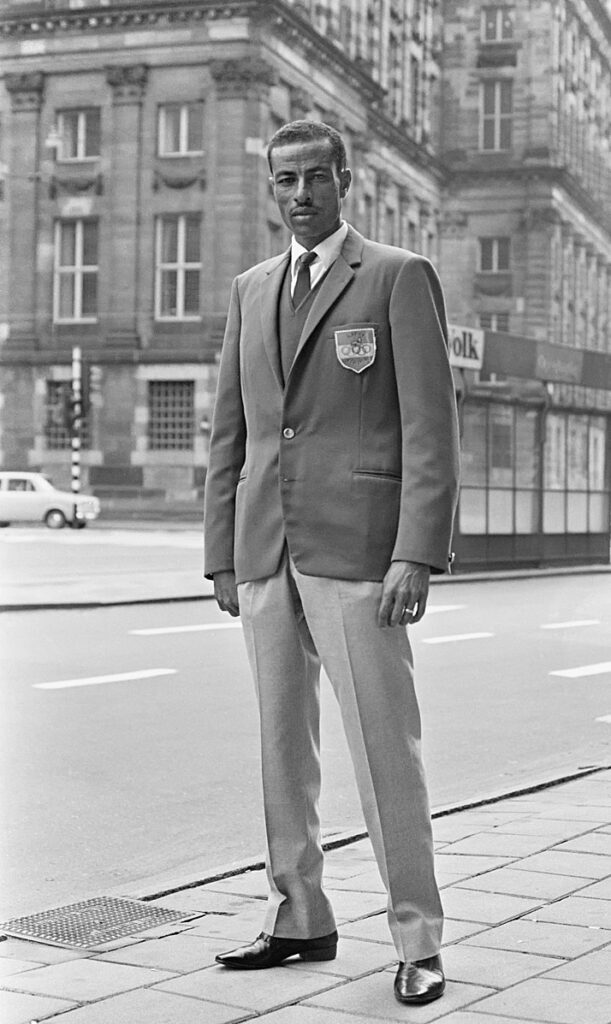 Abebe Bikila Abebe Bikila wearing suit standing in city street.