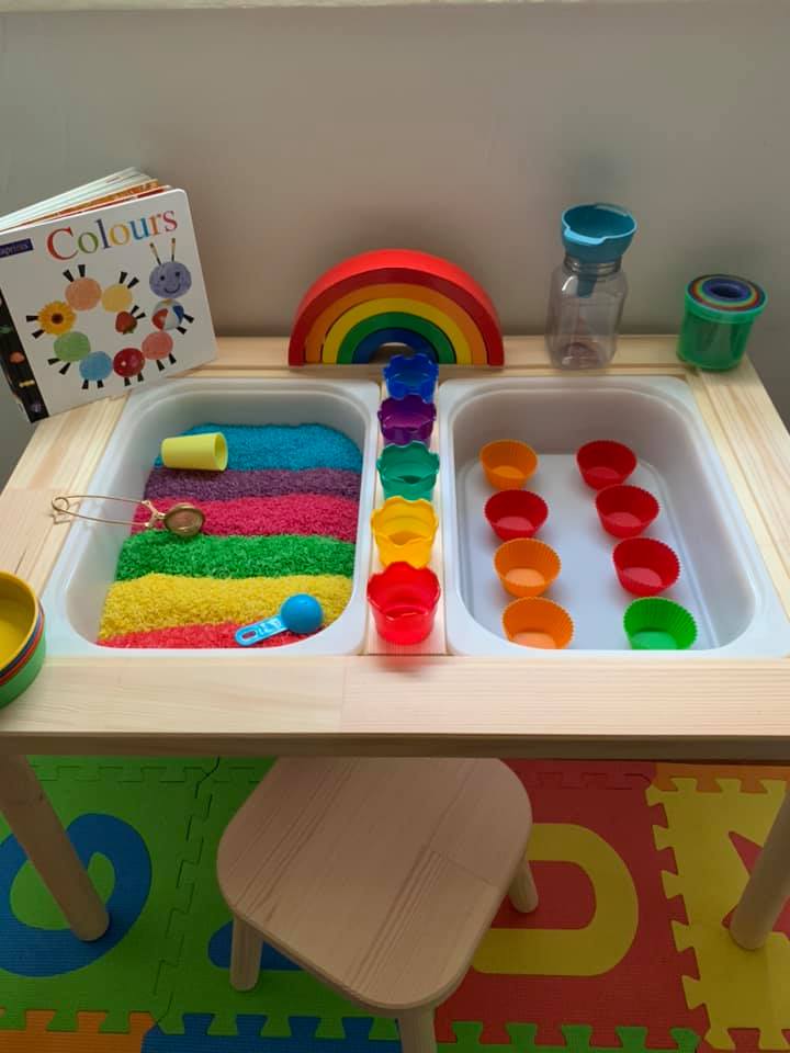A table with two bins inside it is shown. There is rainbow sand on one side in this example of Ikea classroom.