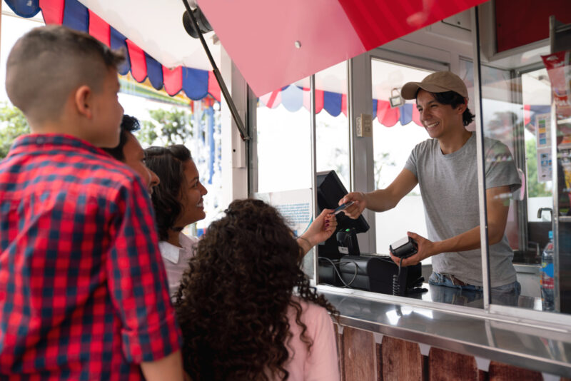 Happy family buying food at an amusement park Portrait of a happy family buying food at an amusement park and paying by card - lifestyle concepts
