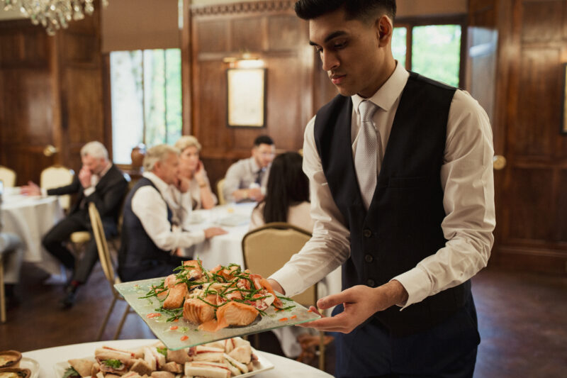Waiter Catering a Business Meeting Waiter holding up a tray with salmon on it ready to setting up food on a buffet table at a business conference.