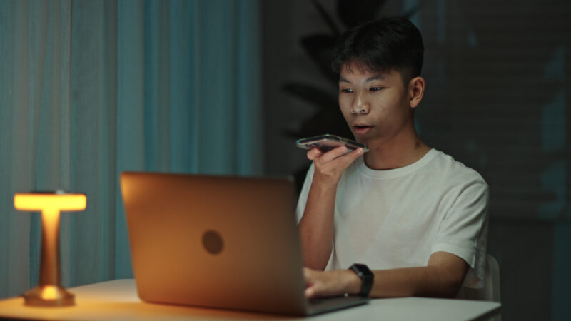 Teenager student talking with a voice assistant on smartphone at night. teenage boy student talking with a voice assistant on smartphone while working at home during night.
