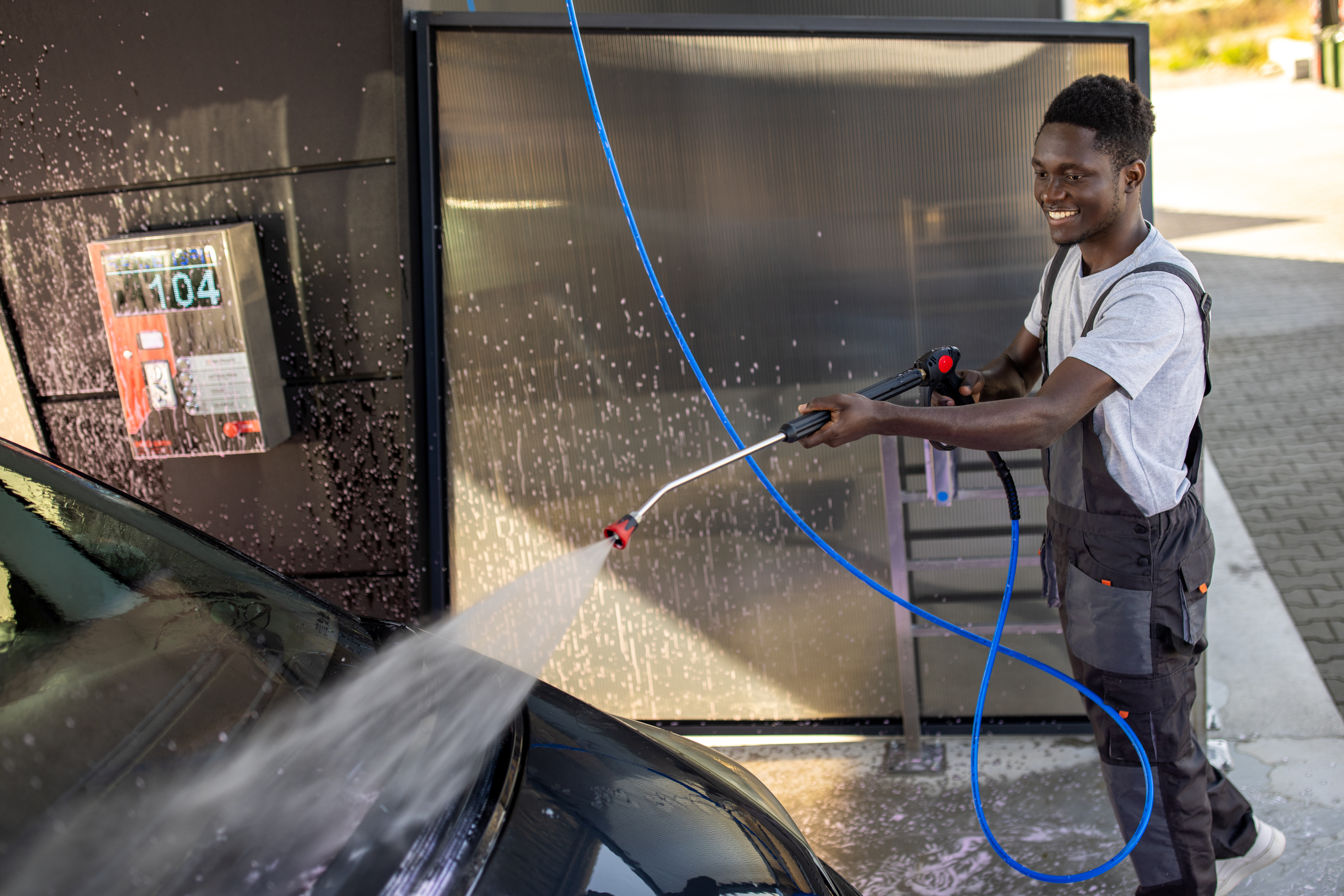Worker Washing Car at Outdoor Service Station Skilled car wash professional sprays a car exterior with precision, using a water cannon.