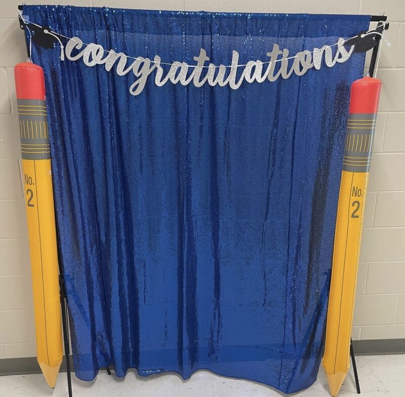 congratulations-sign blue curtain with congratulations written in silver letters and two pencils on either side, teacher hack