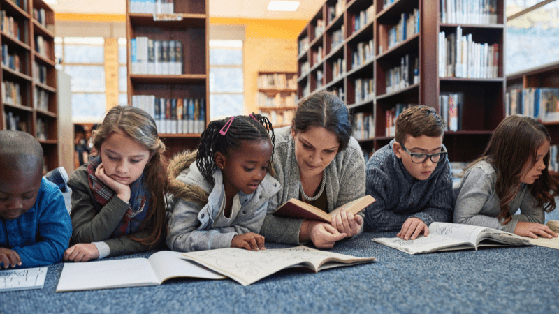 Teacher reading on floor with students to show words to stop using as a teacher