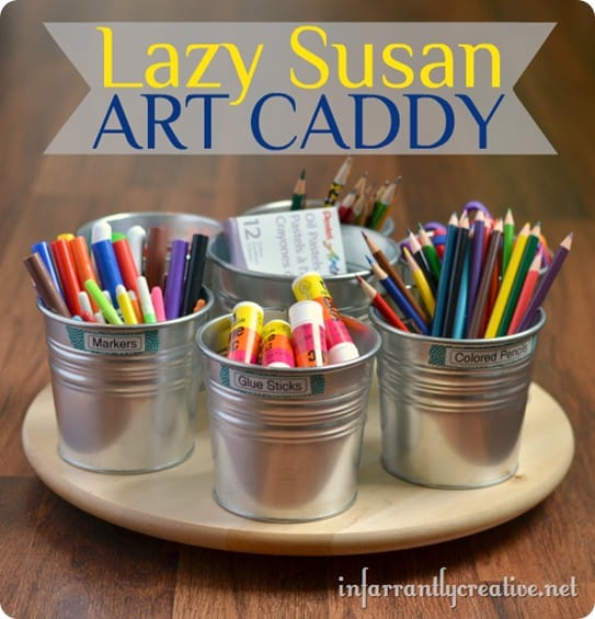 A wooden lazy susan is shown with galvanized pots on it filled with a variety of art supplies.