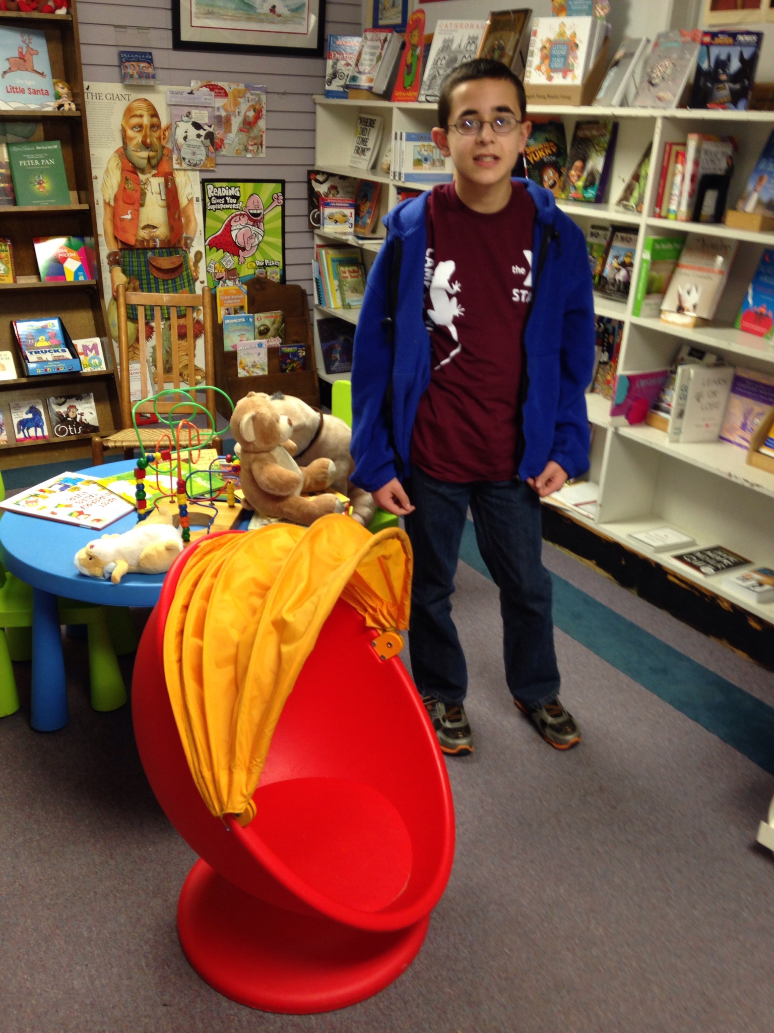 A boy stands in a classroom library. An egg style chair is shown.