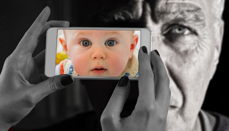 Picture Prompts: Faces Hands holding up a phone with a picture of a baby's face in front an old man's face