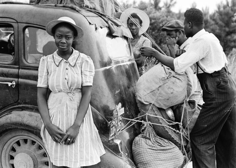 Writing Prompt: Family Travels Vintage photo of a Black family strapping luggage to a car, with a young girl posing in front
