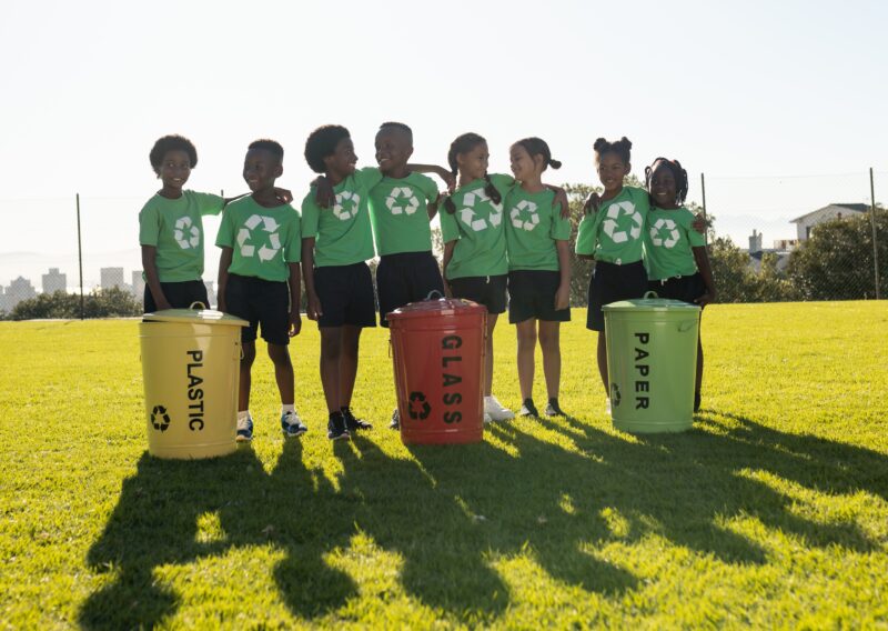Happy diverse children collecting recycling embracing in sunny elementary school field, copy space. Recycling, environment, education, childhood, development, learning and school, unaltered.