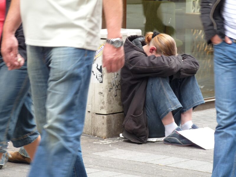 Picture Prompts: Hopeless Woman sitting on a sidewalk with her head on her knees as others walk by