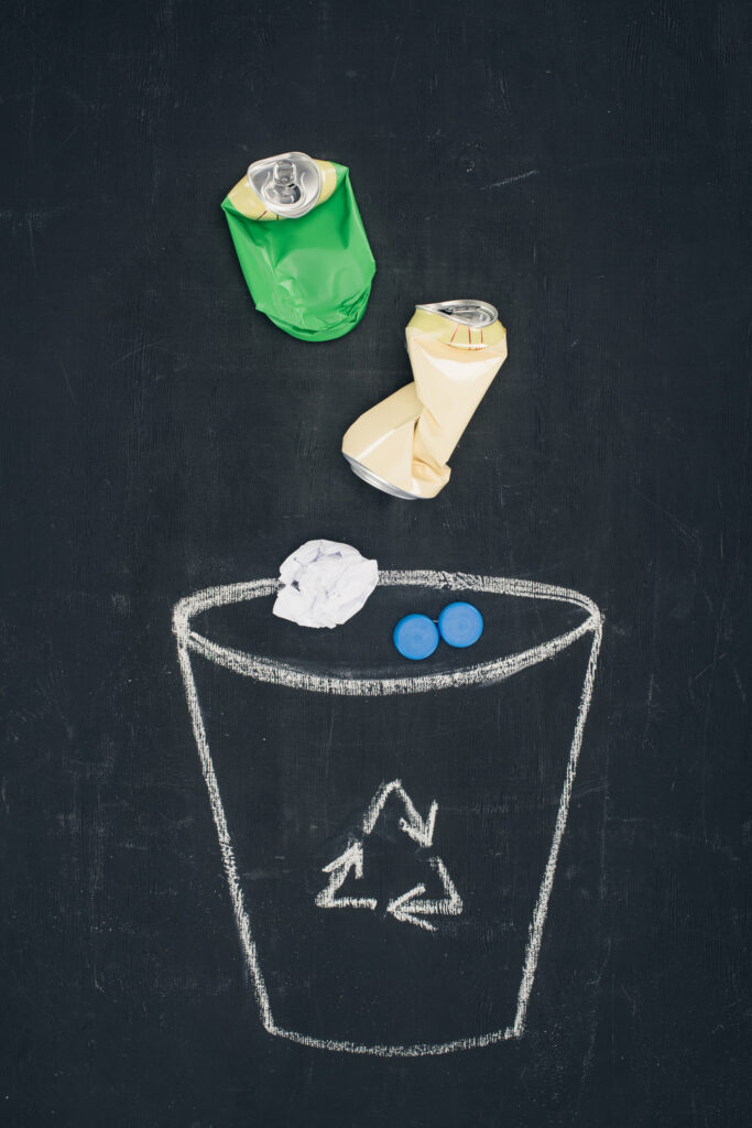 metal cans with crumpled paper falling into drawn trash bin with recycle sign on chalkboard