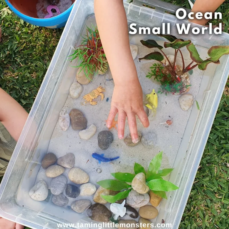 ocean-sensory-bin hands on a bin with water and rocks and ocean toys