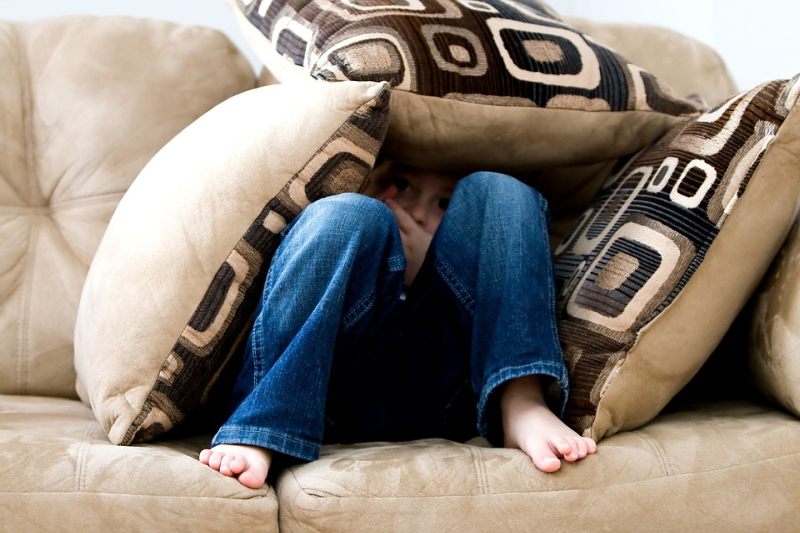 Picture Writing Prompts: Hiding Child Child hiding behind a heap of pillows on a beige couch (Picture Writing Prompts)