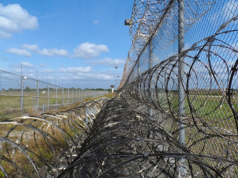 Writing Prompts: Razor Wire A fence topped by rolls of razor wire against a blue sky