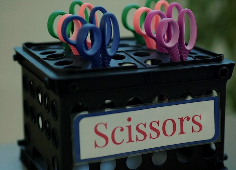 scissors-hack Black storage crate turned upside-down with scissors inserted into the holes, labeled Scissors as an example of dollar store hacks for the classroom