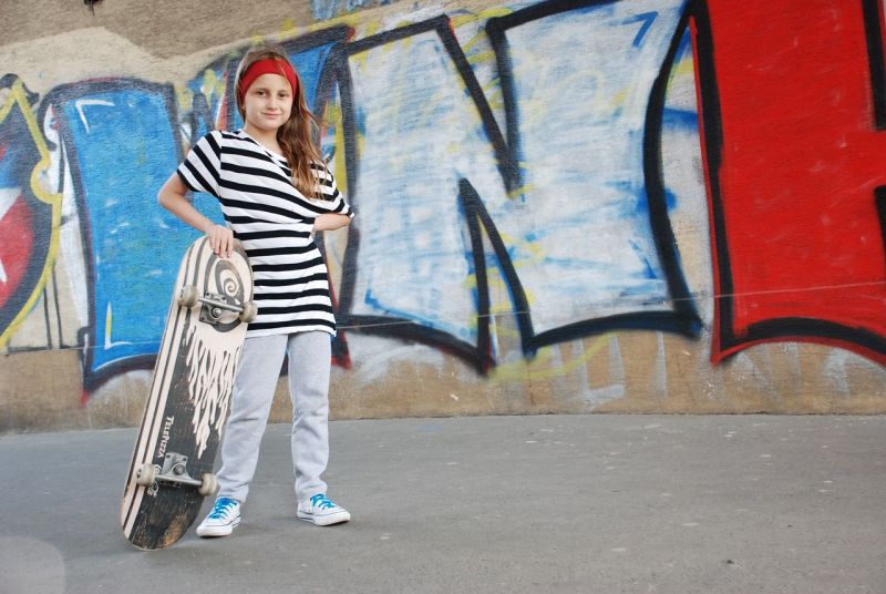 Picture Prompts: Skateboard Girl Girl in a striped shirt and red headband posing with a skateboard in front of some graffiti
