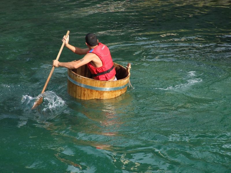 Writing Prompt: Barrel Race Man wearing a life jacket and paddling half a barrel in a lake
