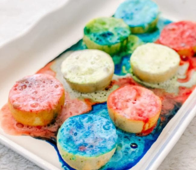 8 lemon halves in a white tray with various colors of fizzing foam on top (Volcano Science Experiments)
