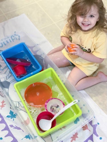 wash-dishes-bin child with two bins filled with water and dishes for water activity washing dishes