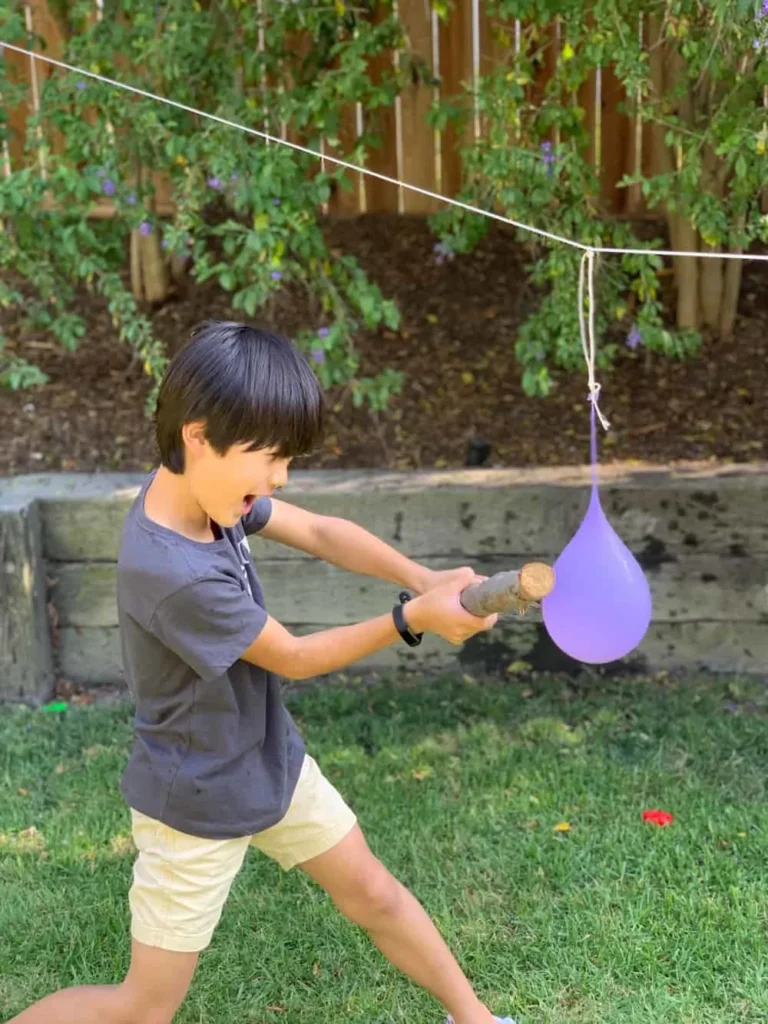 Water Balloon Pinata A boy swinging at a water balloon hung from a clothesline as an example of fun last day of school activities